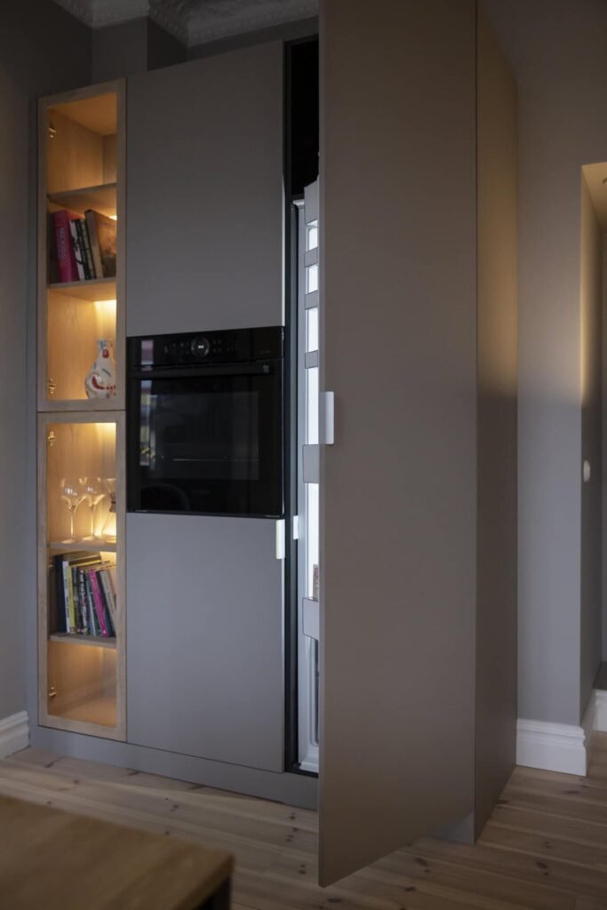 Stiligt - Snyggt, stiligt modernt köksskåp med öppen dörr avslöjar ett integrerat kylskåp. Hyllor med böcker och glas syns till vänster.