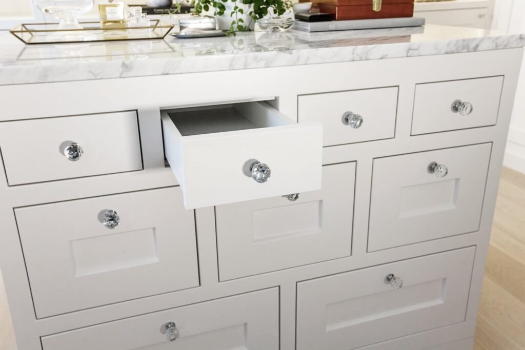 Stiligt - En vit köksö med bänkskiva i marmor utstrålar stiligt charm, med flera lådor. En låda är delvis öppen och har ett tydligt handtag.