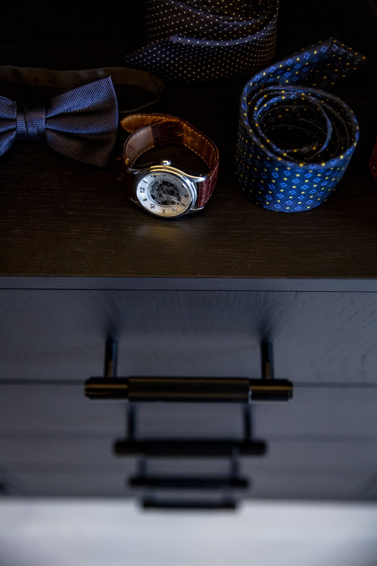 Stiligt -Svart Walk in closet En stiligt låda med ett armbandsur, snyggt rullade slipsar och en elegant fluga till vänster.