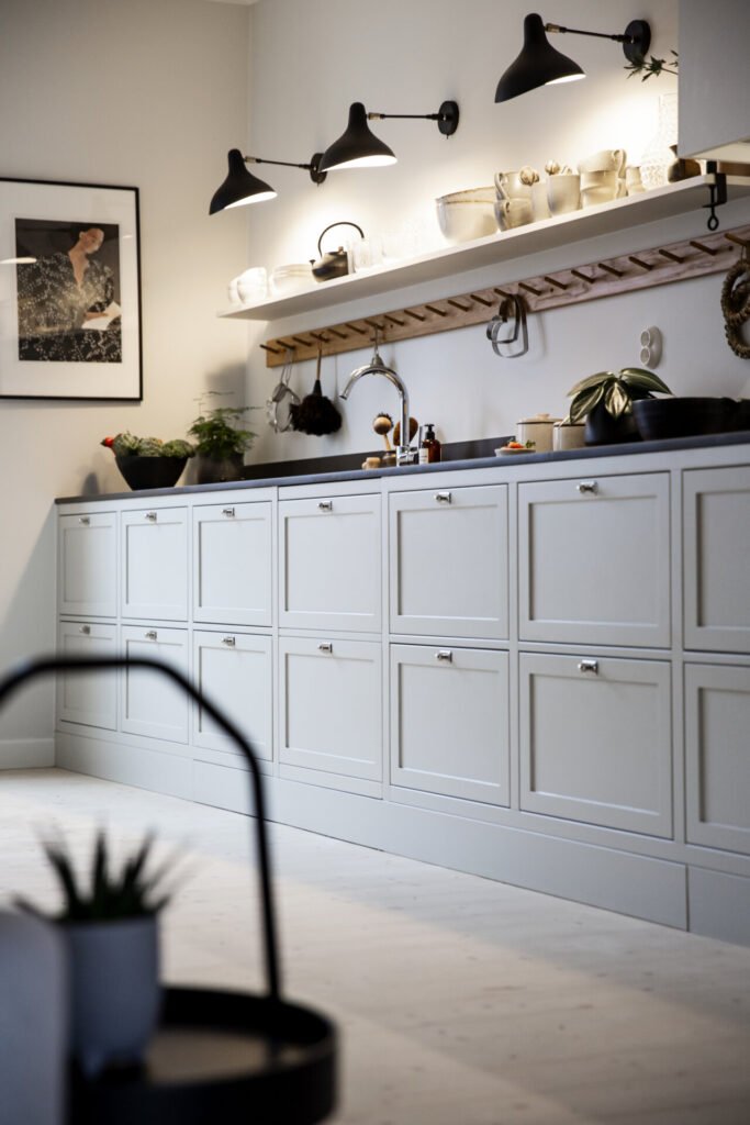 Stiligt - Minimalistiskt kök med stiligt vita skåp, svart bänkskiva, vägghängda hyllor och moderna svarta armaturer. En inramad konst hänger på väggen.