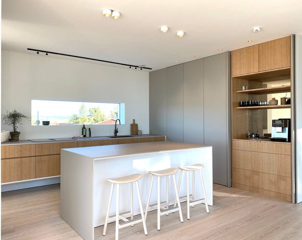 Stiligt - Modernt kök med en stiligt ö, tre pallar, träskåp, inbyggda vitvaror och ett stort fönster som ger naturligt ljus.
