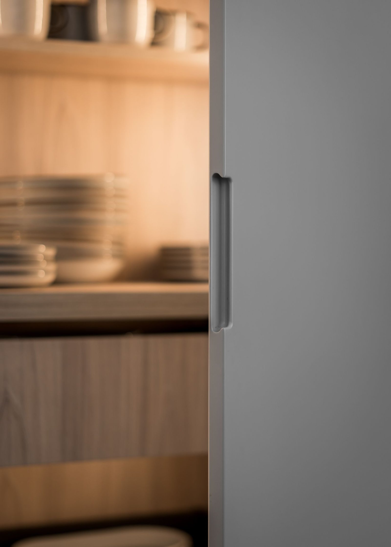 Stiligt - En närbild av ett stiligt öppet köksskåp med prydligt staplade tallrikar och skålar inuti, upplyst av varmt ljus.