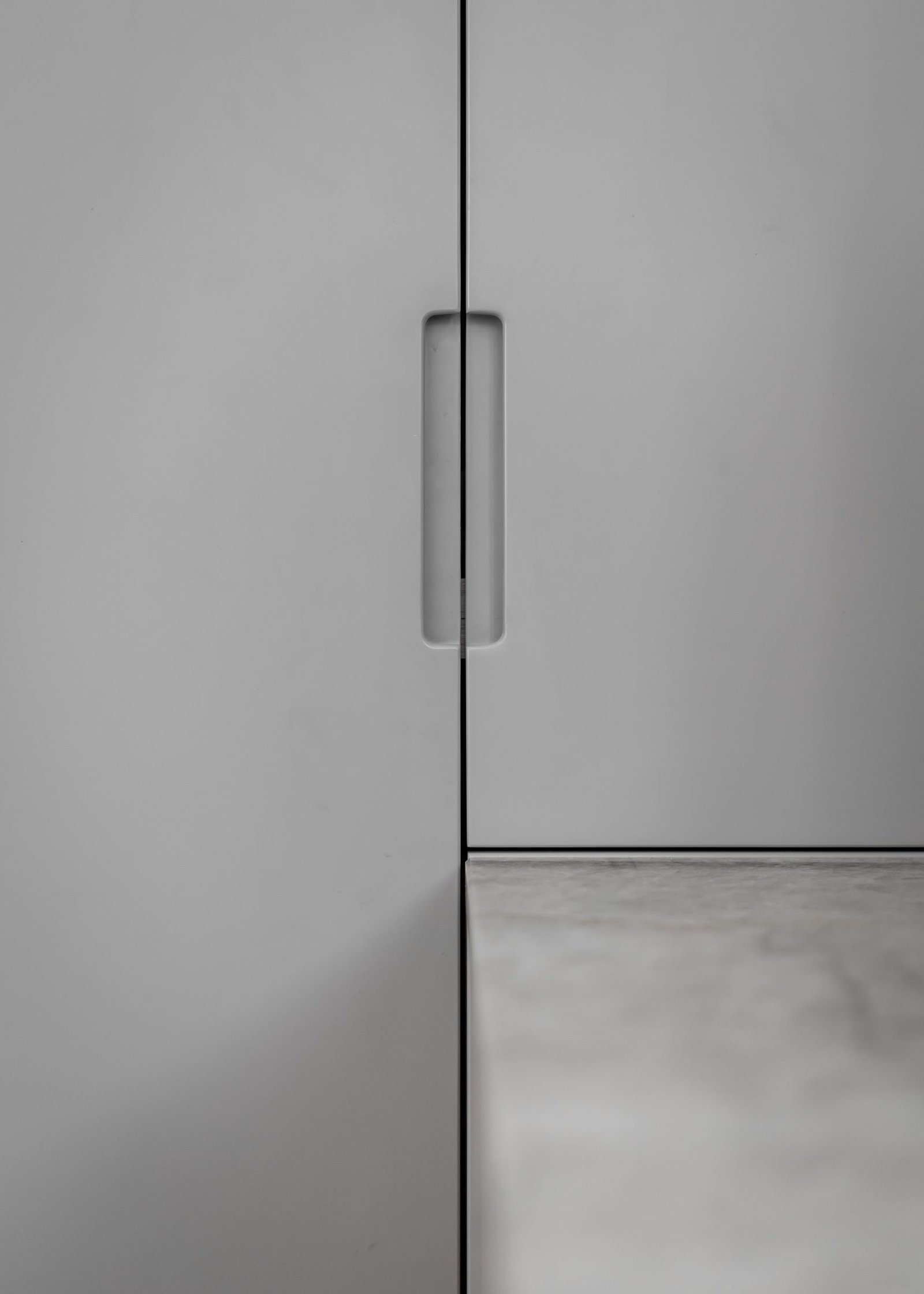 Stiligt - Närbild av en stiligt grå skåpdörr, med ett infällt vertikalt handtag och den synliga kanten av en snygg bänkskiva till höger.