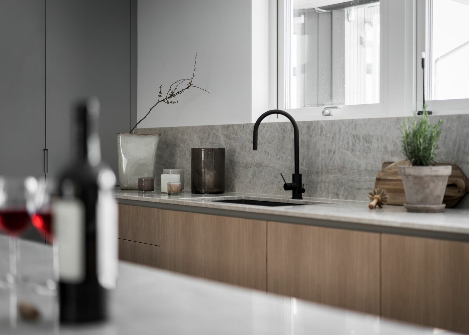 Stiligt - Minimalistiskt kök med stiligt ljusa träskåp, en elegant svart kran, dekorativa växter och en vinflaska elegant placerad på bänken.