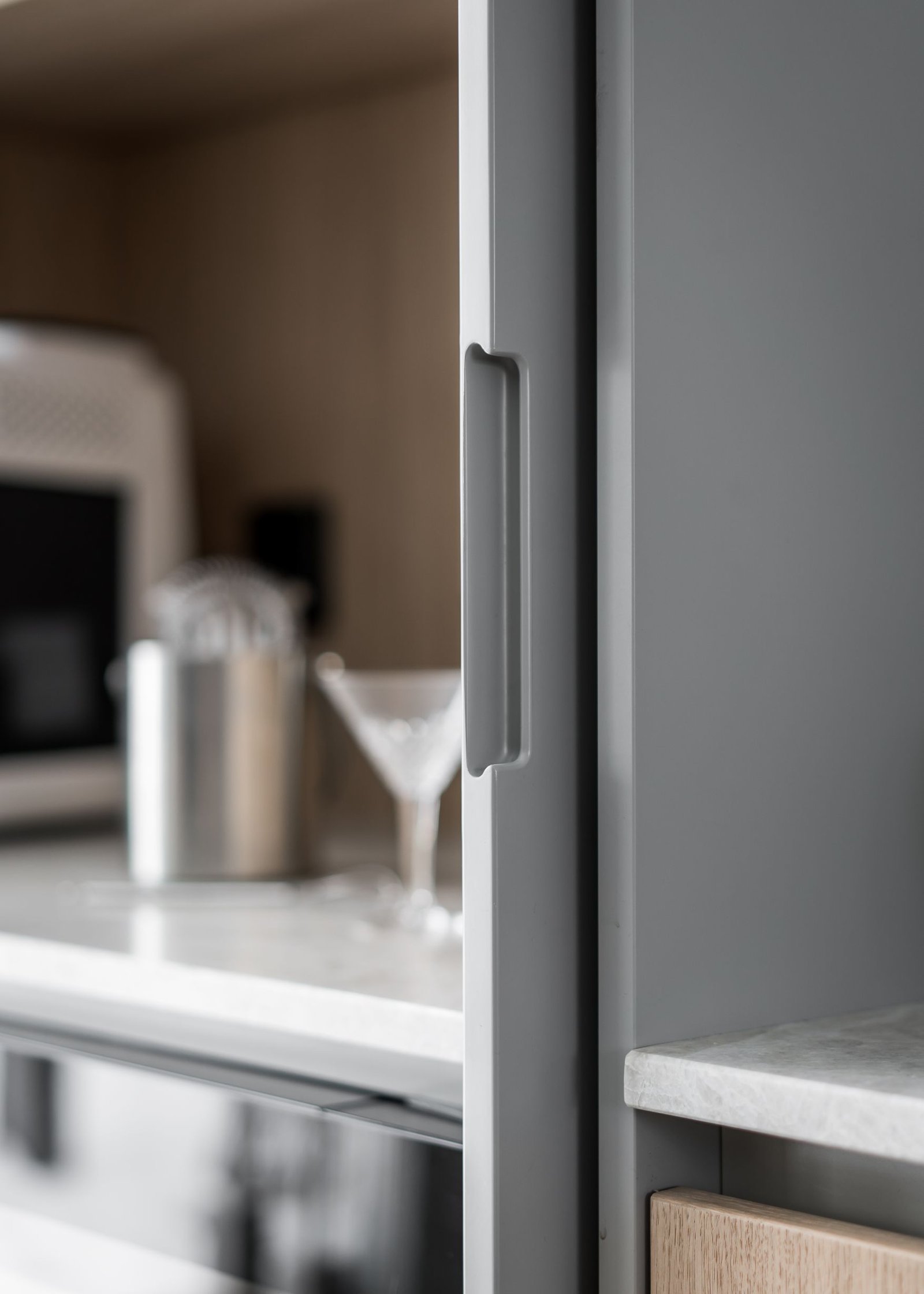 Stiligt - Närbild av ett stilrent modernt kök med metallskåpshandtag, bänkskivor i marmor, en redskapshållare i rostfritt stål och ett elegant glas med skaft på bänken.