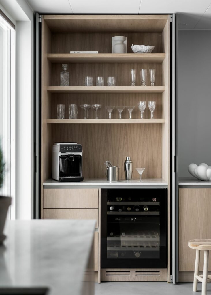 Stiligt - Stiligt köksskåp med öppna hyllor visar konstfullt glas och kaffebryggare. Nedanför är snygga lådor och ett litet kylskåp sömlöst integrerade i träskåpet.