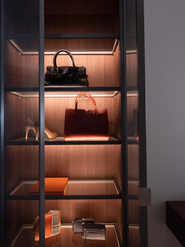 Stiligt - Ett stiligt vitrinskåp med trähyllor visar upp en elegant kollektion av handväskor, höga klackar och små accessoarer.