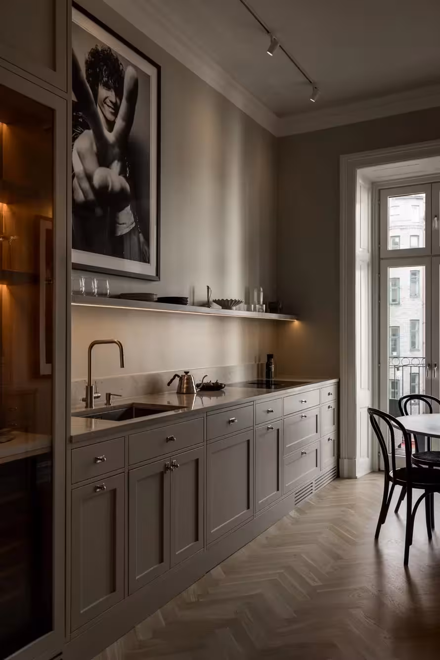 Stiligt - Modernt kök i shakerstil med ljusgrå skåp, mässingsarmaturer, öppna hyllor och ett stort svartvitt foto ovanför diskbänken; ett runt bord och stolar står nära ett högt fönster.