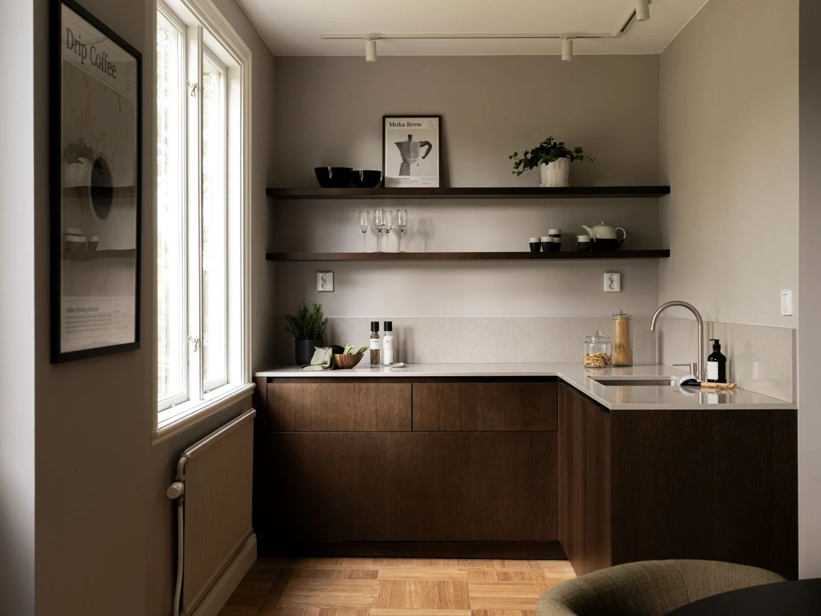 Stiligt - Ett minimalistiskt träkök med skjutdörrar, bruna skåp, öppna hyllor med porslin och prydnadsföremål, en diskho, prylar på bänkskivan samt ett stort fönster som släpper in naturligt ljus.