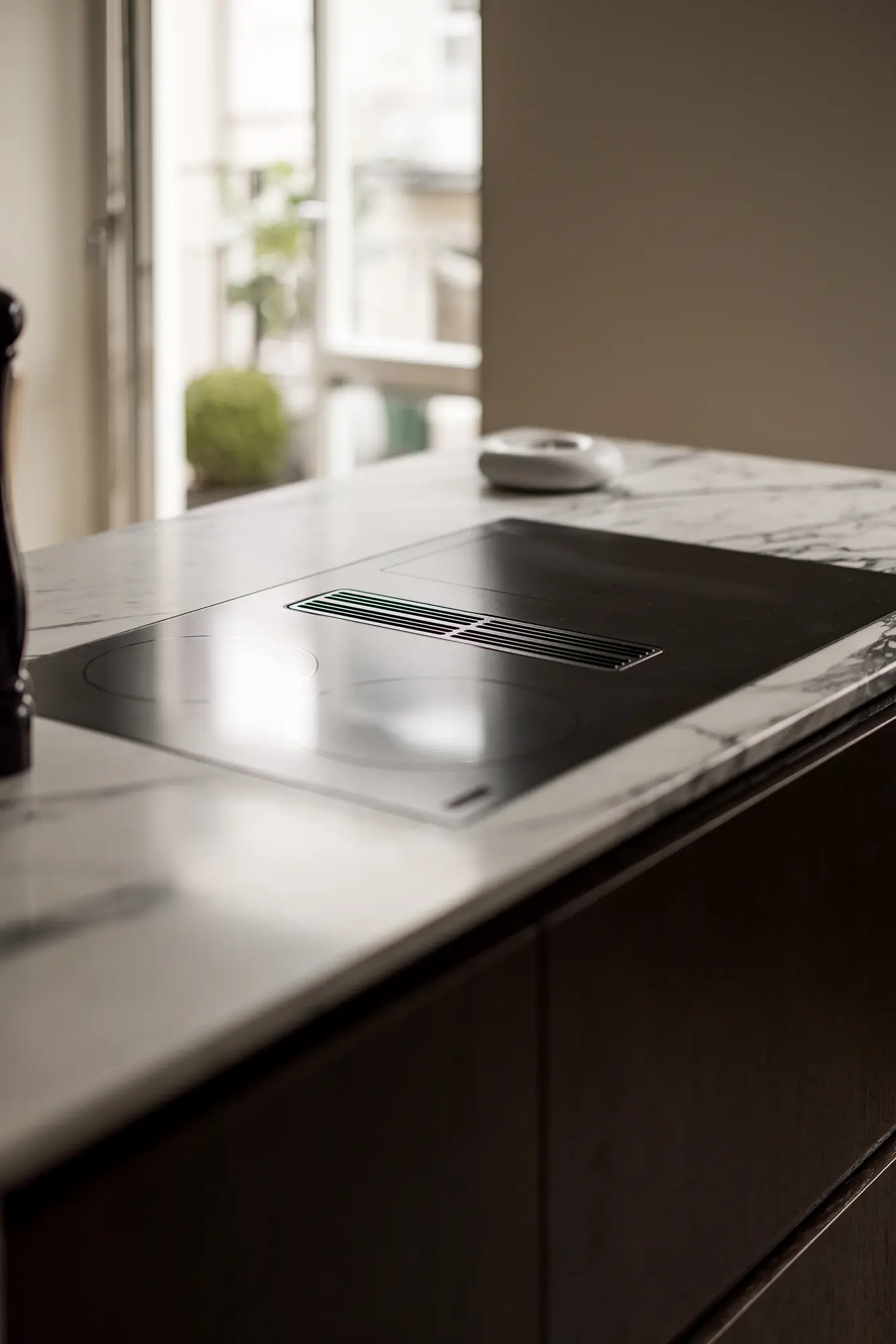 Stiligt - En modern köksö har en svart induktionshäll som är sömlöst integrerad i en bänkskiva i vit marmor, perfekt placerad framför ett öppet fönster.