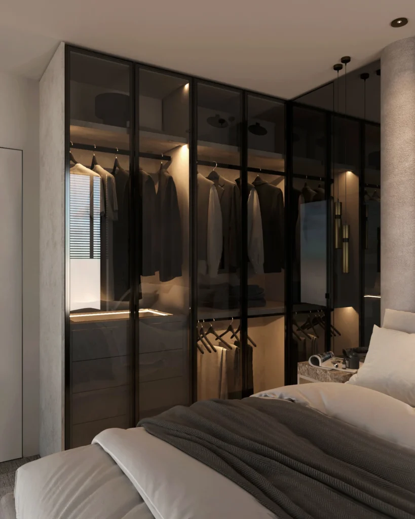 Stiligt - Ett modernt sovrum med en garderob med vitrindörrar som visar hängande kläder, prydligt bäddad säng i förgrunden och minimalistisk inredning med mjuk belysning.