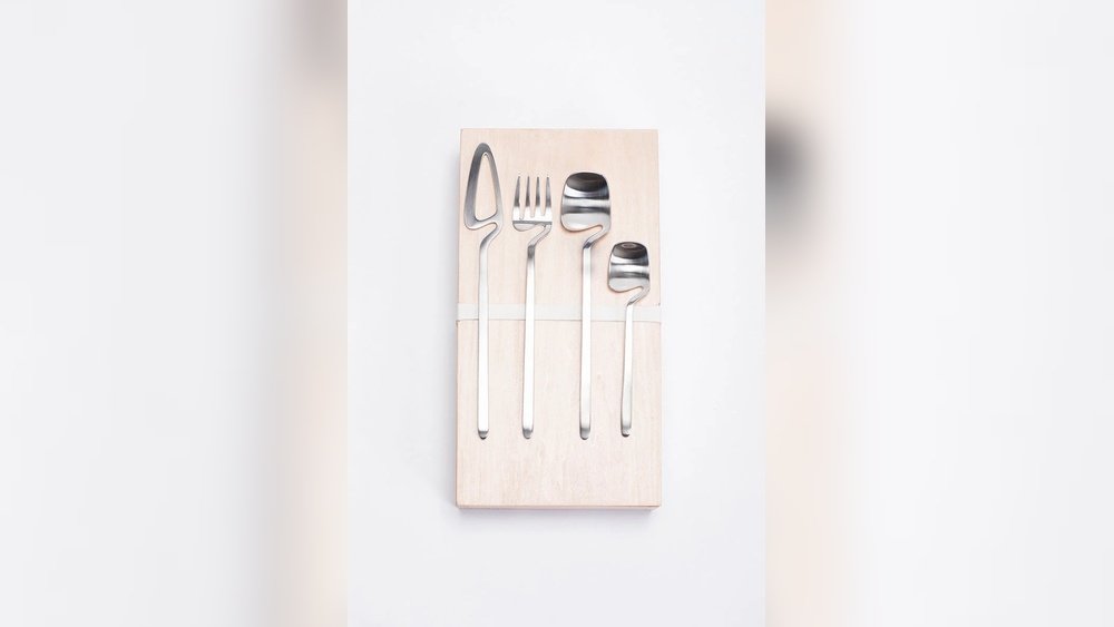 Stiligt - Fyra silverbestick - en sked, en gaffel, en kniv och en mindre sked - är placerade i en rad på en ljus träskiva mot en vit bakgrund.