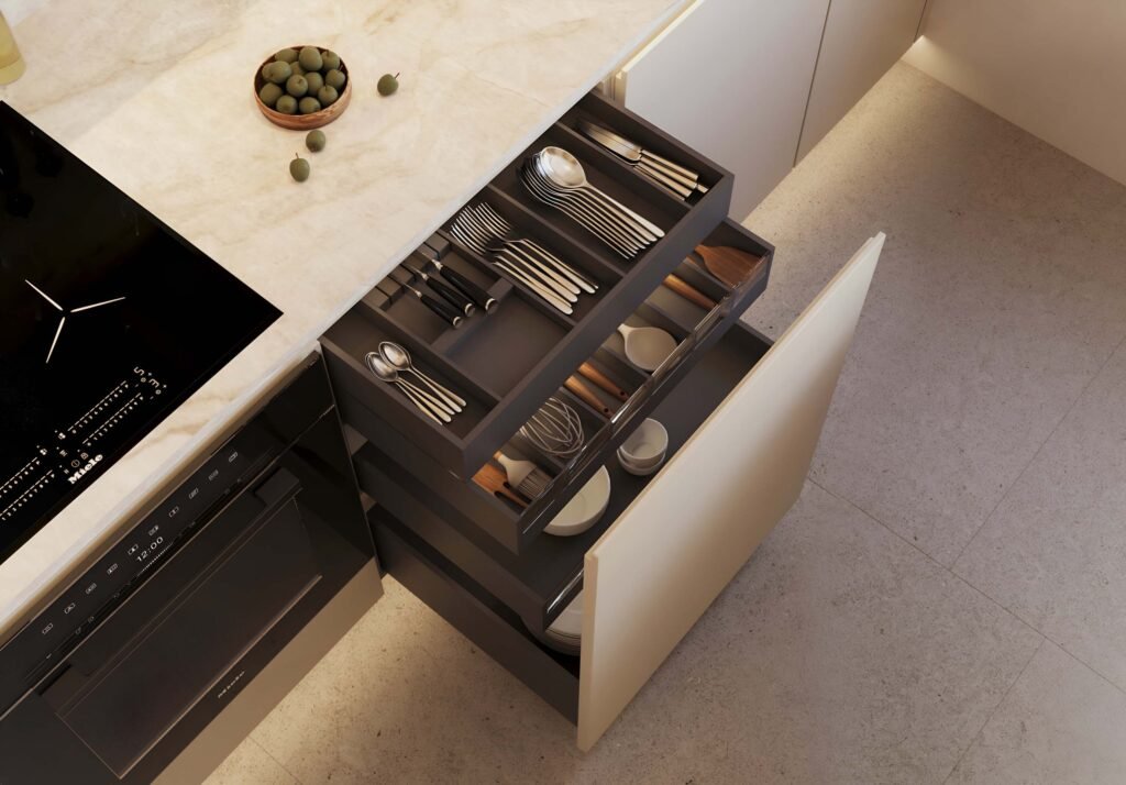 Stiligt - En kökslåda är öppen och avslöjar organiserade fack med bestick, köksredskap, tallrikar och skålar. På bänkskivan ovanför står en skål med gröna oliver. Undvik att köket känns trångt & mörkt 