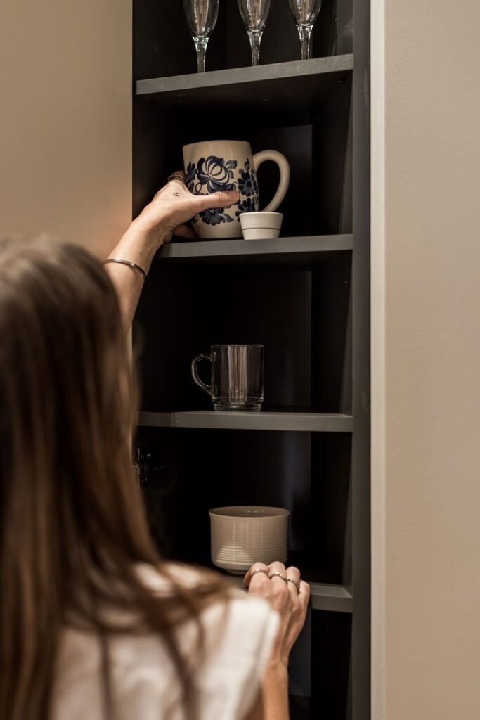 Stiligt - En person placerar en mugg med blått blommönster på en hylla i ett skåp med glas, andra muggar och smarta dolda lådor hörnlösningar för extra förvaring. Dolda lådor och smarta hörnlösningardu inte visste fanns: Maxa plats & stil 