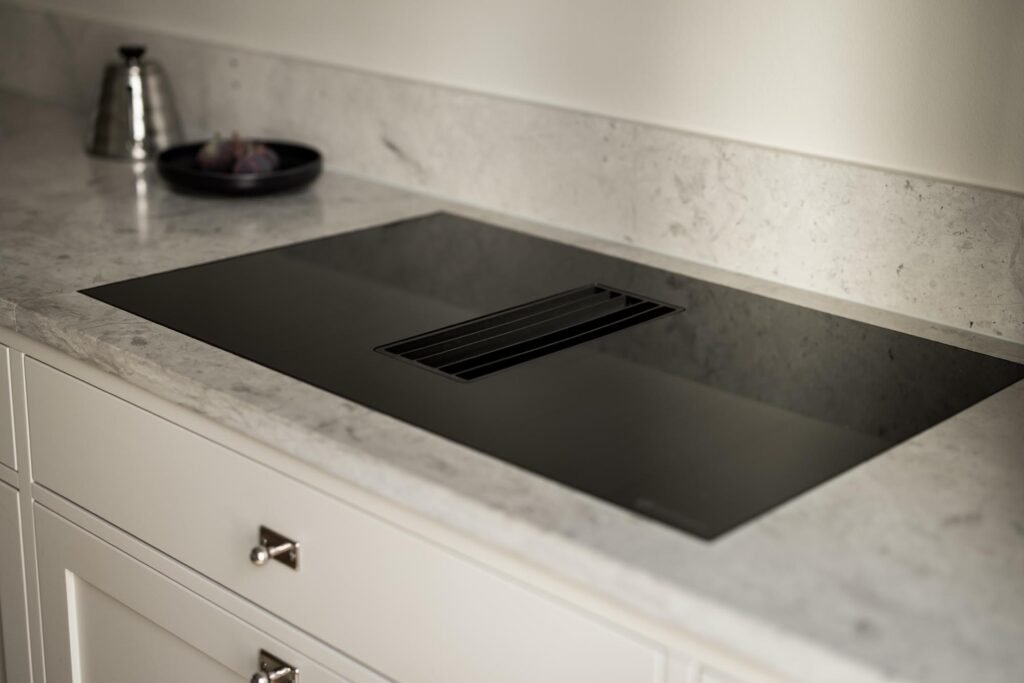 Stiligt - En modern svart induktionshäll med integrerad ventil är installerad på en bänkskiva i vit marmor i ett modernt kök. Rätt höjd på bänkskiva, överskåp och köksö: ultimata guiden 2025