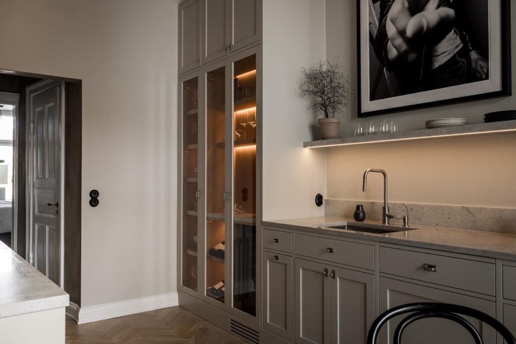 Stiligt - Modernt pentry med grå skåp, vitrinskåp med glasfront, bänkskiva i marmor, liten diskho, hylla med glasögon, krukväxt och svartvitt foto på väggen. 5 kostnadsfällor att undvika vid köksrenovering: Spara stort!