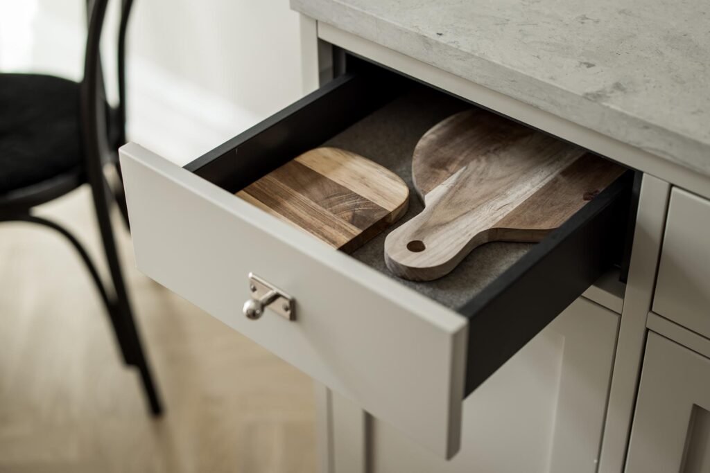 Stiligt - En öppen kökslåda med två skärbrädor i trä under en grå bänkskiva, med en del av en svart stol synlig i bakgrunden. Underskåp kontra lådor - vad är mest ergonomiskt? Maximal komfort
