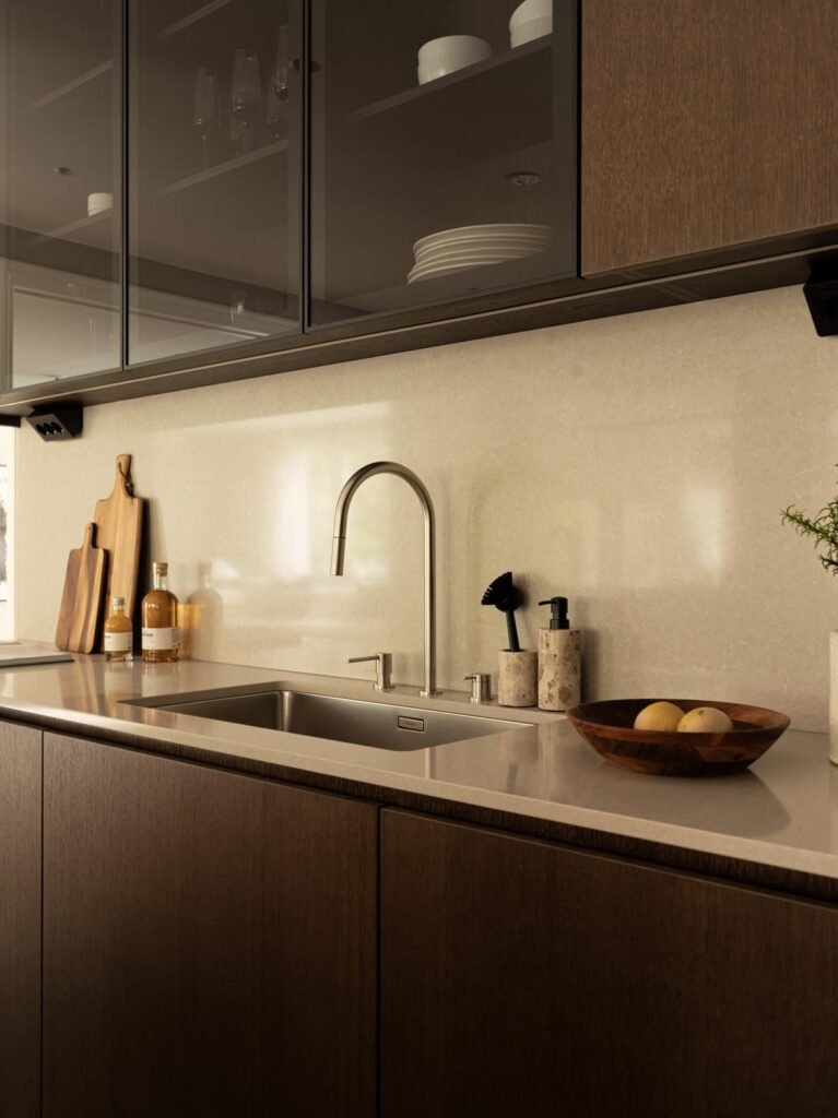 Stiligt - Modern köksbänk med diskho i rostfritt stål, hög kran, tvåldispenser, skärbrädor, flaskor och en skål med citroner - en elegant Köksdesign i Stockholm under vitrinskåpen. Köksdesign Stockholm: Inspirerande ideer för ditt drömkök