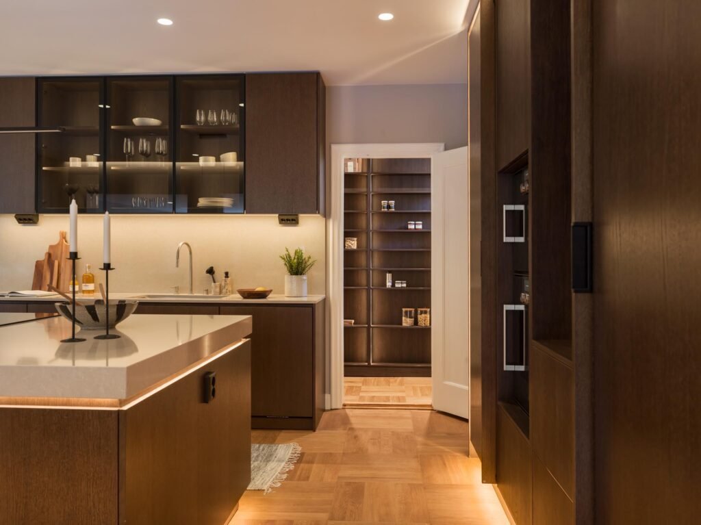 Stiligt - Modernt kök med skåp i mörkt trä, ljusa bänkskivor, en köksö med en ljusstake i mitten och ett öppet skafferi. Varm, mjuk belysning förhöjer denna eleganta köksdesign i Stockholm. Köksdesign Stockholm: inspirerande ideer för ditt drömkök!