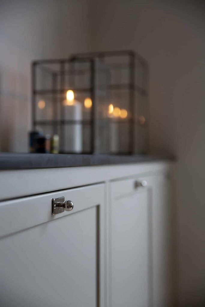 Stiligt - Närbild på vita skåpluckor med metallknoppar, toppade med glaslyktor med tända ljus. De vackraste kulörerna för platsbyggda kök just nu: Trendiga färger 2025