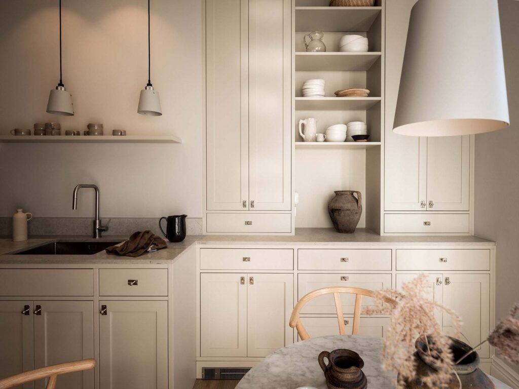 Stiligt - Minimalistiskt kök med krämfärgade skåp från koksdesign-göteborg, öppna hyllor med disk, diskho och ett runt bord med torkade blommor i förgrunden. Köksdesign Göteborg: inspirerande ideer för ditt drömkök