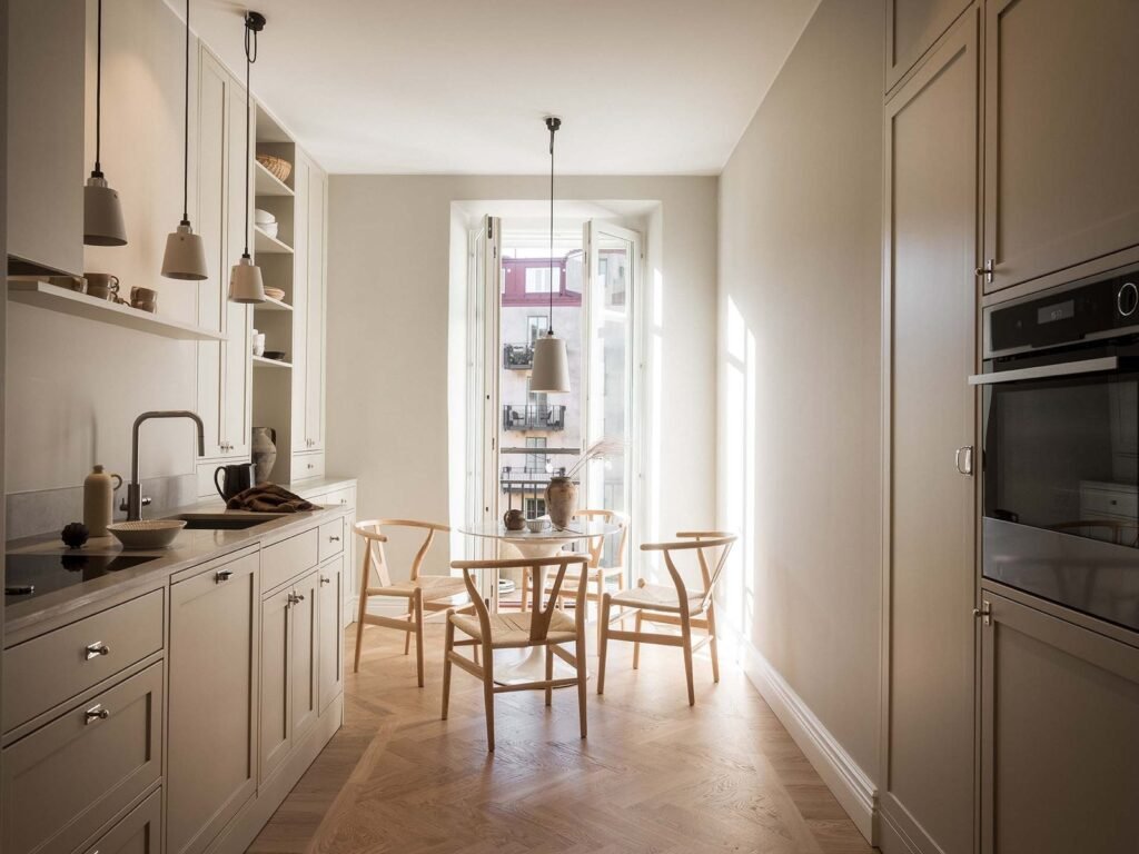 Stiligt - Ett modernt, minimalistiskt kök med skåp i ljust trä, inbyggda vitvaror och ett runt matbord med fyra stolar nära ett fönster som släpper in naturligt ljus - perfekt för Shakerkök-inspiration. Shakerkök inspiration: stilrena ideer för ditt drömkök