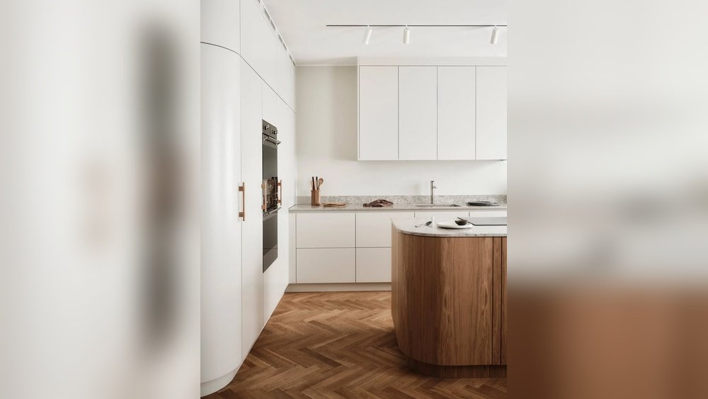 Stiligt - Modernt kök med vita skåp, inbyggd ugn, bänkskivor i marmor och en köksö i trä på ett fiskbensmönstrat trägolv.