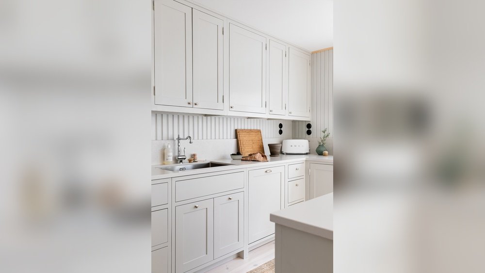 Stiligt - Ett modernt kök med vita skåp, en bänkskiva med diskho, en skärbräda, en brödrost och minimal inredning.