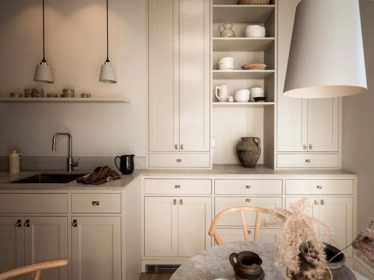 Stiligt - Ett neutralt kök med krämfärgade skåp, öppna hyllor med disk, diskho, pendellampor och ett runt bord med stolar i förgrunden. Att välja färg i nya köket: Experttips för perfekt stil
