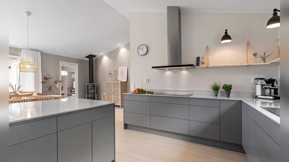 Stiligt - Modernt kök med grå skåp, vita bänkskivor, väggklocka och belysning under skåpen. Öppna hyllor med glas och köksartiklar; matplatsen syns i bakgrunden.