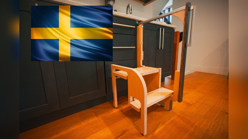 Stiligt - Ett lärandetorn i trä är placerat på ett köksgolv bredvid skåp; en svensk flagga visas i bildens övre vänstra hörn.