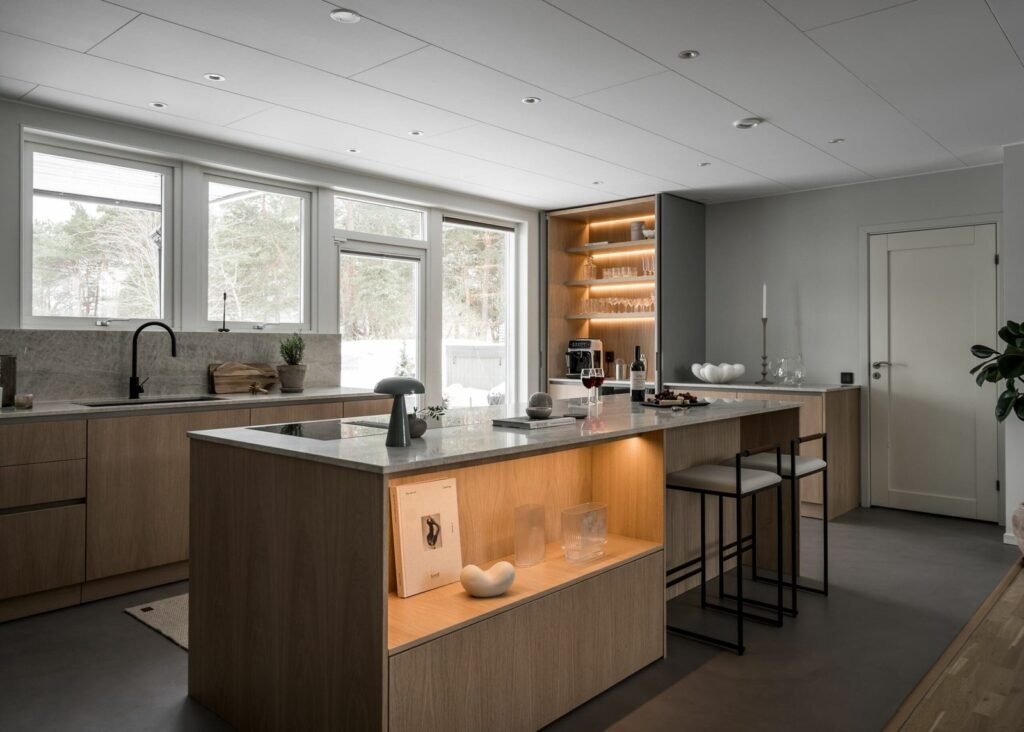 Stiligt - Modernt kök med skåp i ljust trä, bänkskivor i marmor, sittö, öppna hyllor med glasföremål och stora fönster som ger naturligt ljus. Modern skandinavisk design i platsbyggt kök - minimalist med värme: stilrent & inbjudande