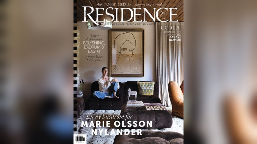 Stiligt - En kvinna sitter i en m&ouml;rk soffa i ett stilfullt vardagsrum med modern inredning och ett stort minimalistiskt portr&auml;tt p&aring; v&auml;ggen. Scenen &auml;r p&aring; omslaget till tidningen Residence.