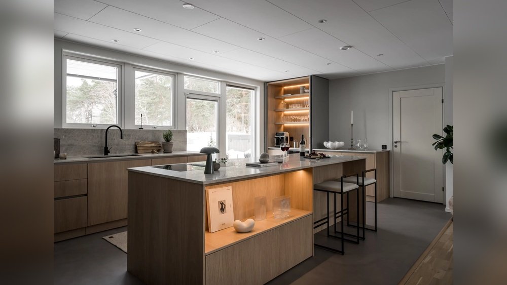 Stiligt - Modernt kök med skåpinredning i ljust trä, bänkskivor i marmor, inbyggda hyllor, barstolar och stora fönster som släpper in naturligt ljus.