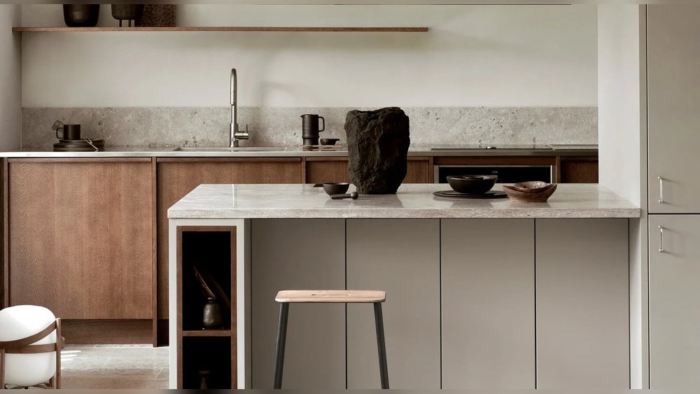 Stiligt - Modernt kök med träskåp, en central ö med en stenbänkskiva, en enda pall och minimalistisk inredning inklusive en stor mörk sten i mitten.