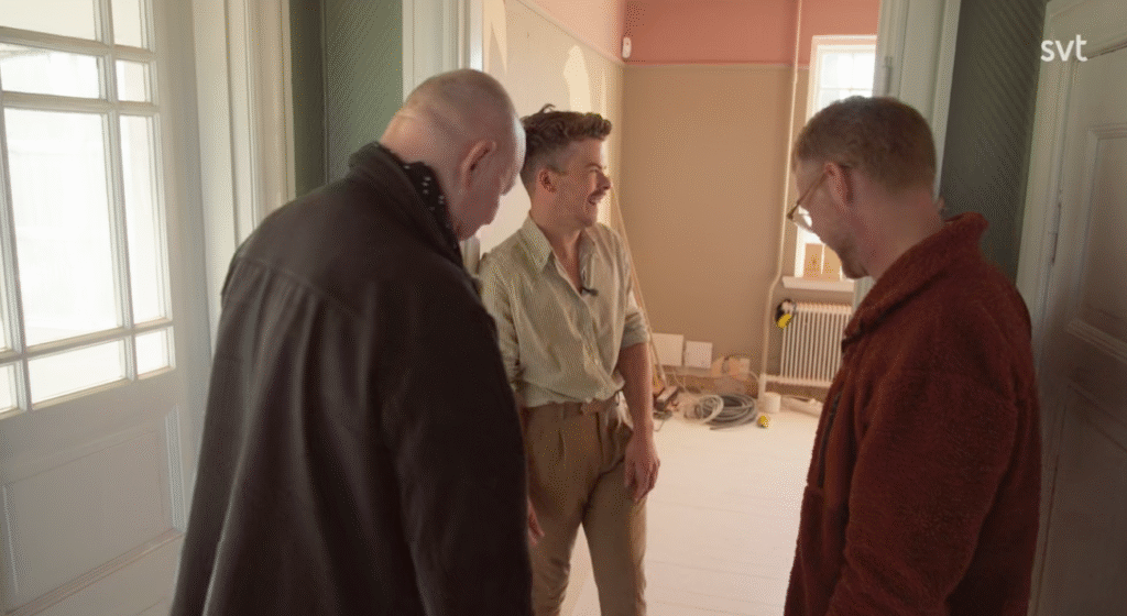 Stiligt - Tre personer står i ett starkt upplyst, delvis renoverat rum, med verktyg och material synliga i bakgrunden.