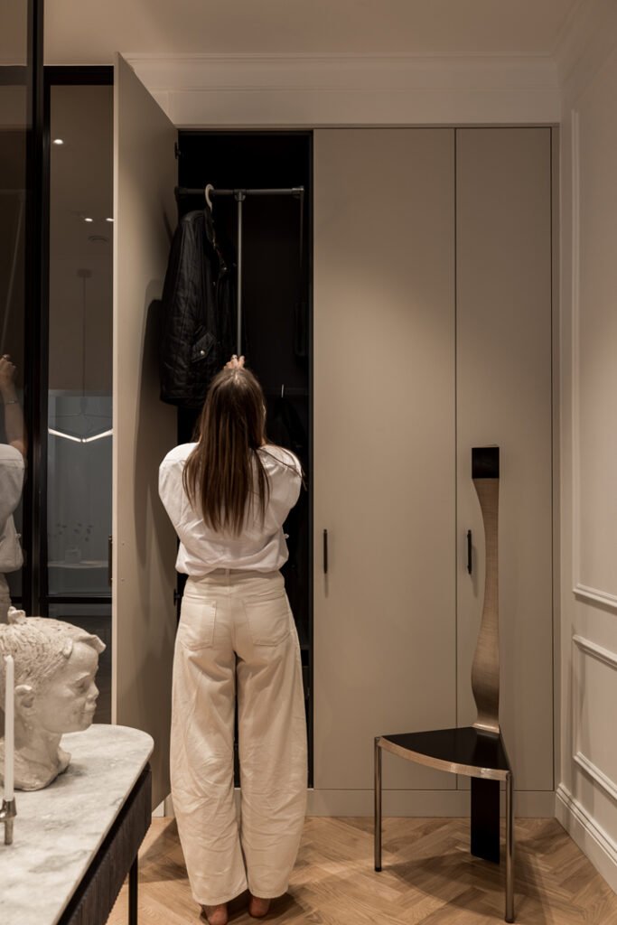 Stiligt - En person i vita byxor och vit skjorta står framför en öppen garderob och inspekterar eller organiserar föremålen i garderoben.