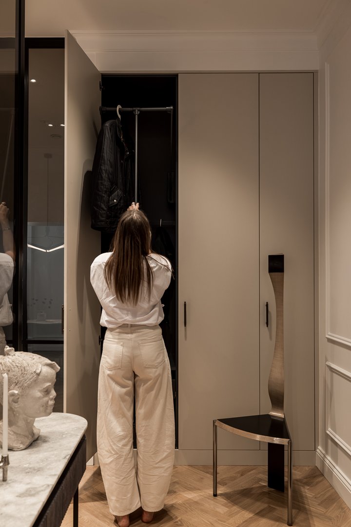 Stiligt - En person i vita byxor och vit skjorta står framför en öppen garderob och inspekterar eller organiserar föremålen i garderoben.