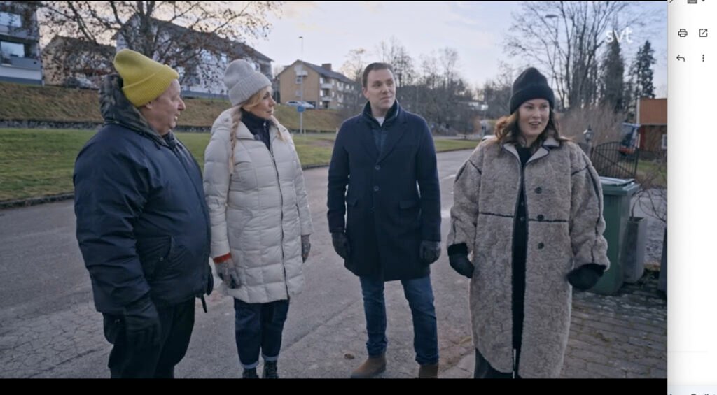 Stiligt - Fyra vinterklädda vuxna står ute på en bostadsgata och pratar. Träd och flerfamiljshus syns i bakgrunden.