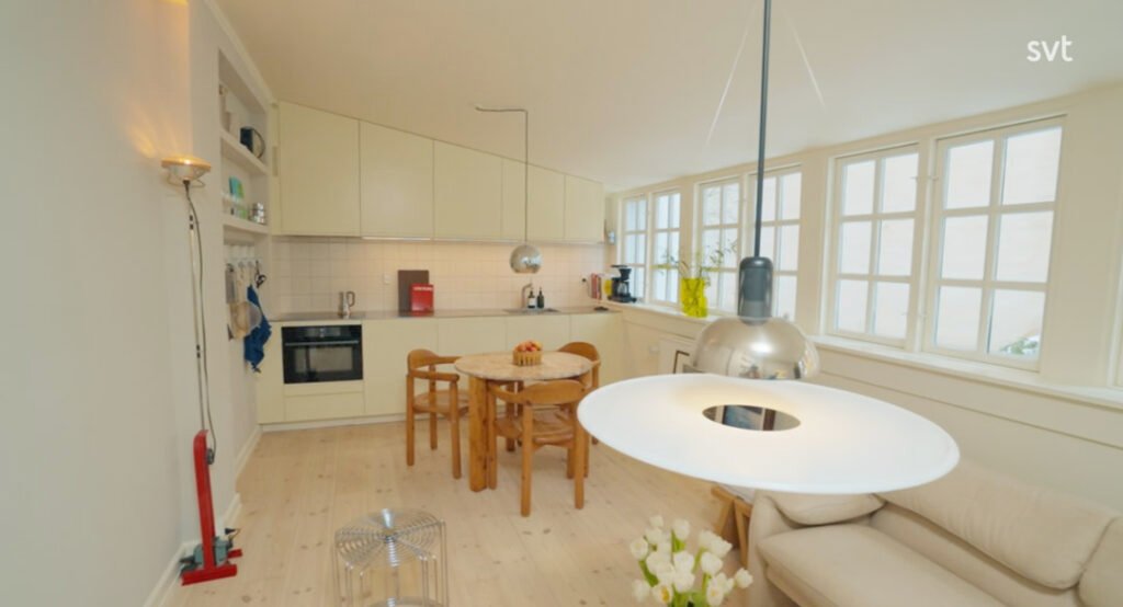 Stiligt - Ett modernt kök och matplats med ljusa trägolv, krämfärgade skåp, ett runt bord med trästolar, stora fönster och pendellampor.