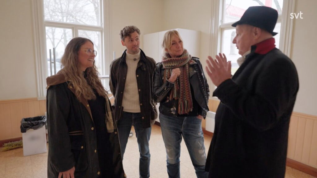 Stiligt - Fyra personer står i ett rum och samtalar; en person gestikulerar med händerna medan de andra lyssnar.