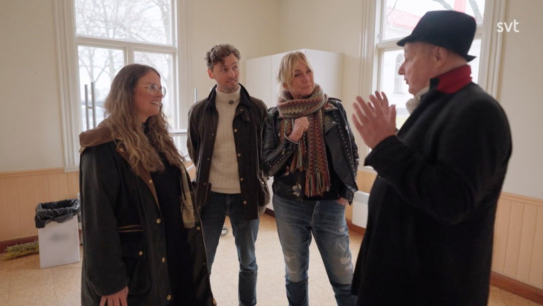 Stiligt - Fyra personer står i ett rum och samtalar; en person gestikulerar med händerna medan de andra lyssnar.