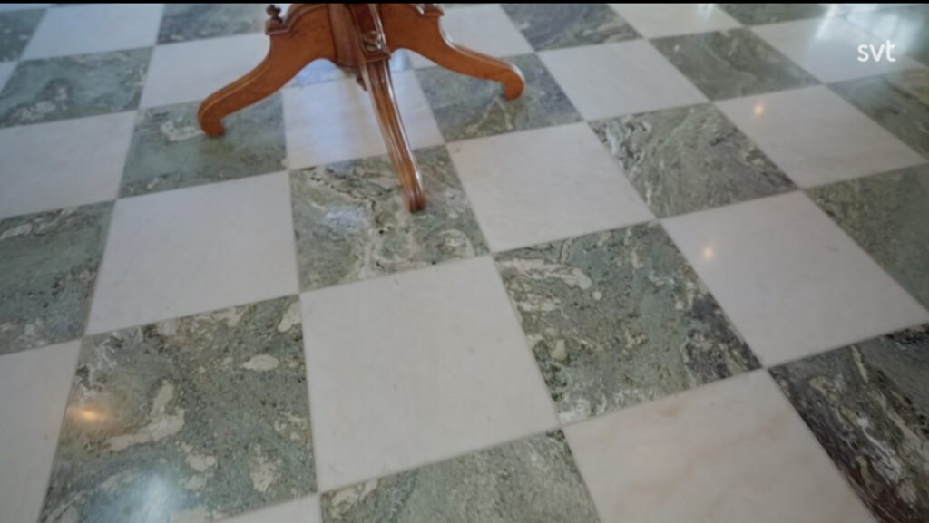 Stiligt - Schackrutigt marmorgolv med omväxlande vita och gröngrå plattor, del av ett träbordsben syns upptill i mitten.