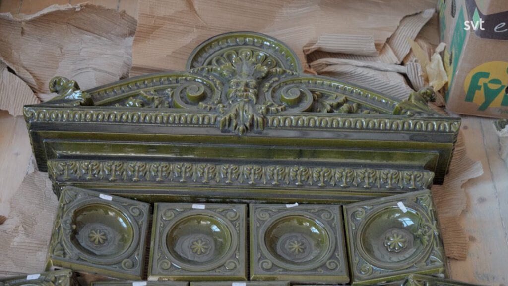 Stiligt - Utsmyckad grön keramikspis med dekorativa mönster och lejonansikte, mot en bakgrund av sönderriven kartong och gips.