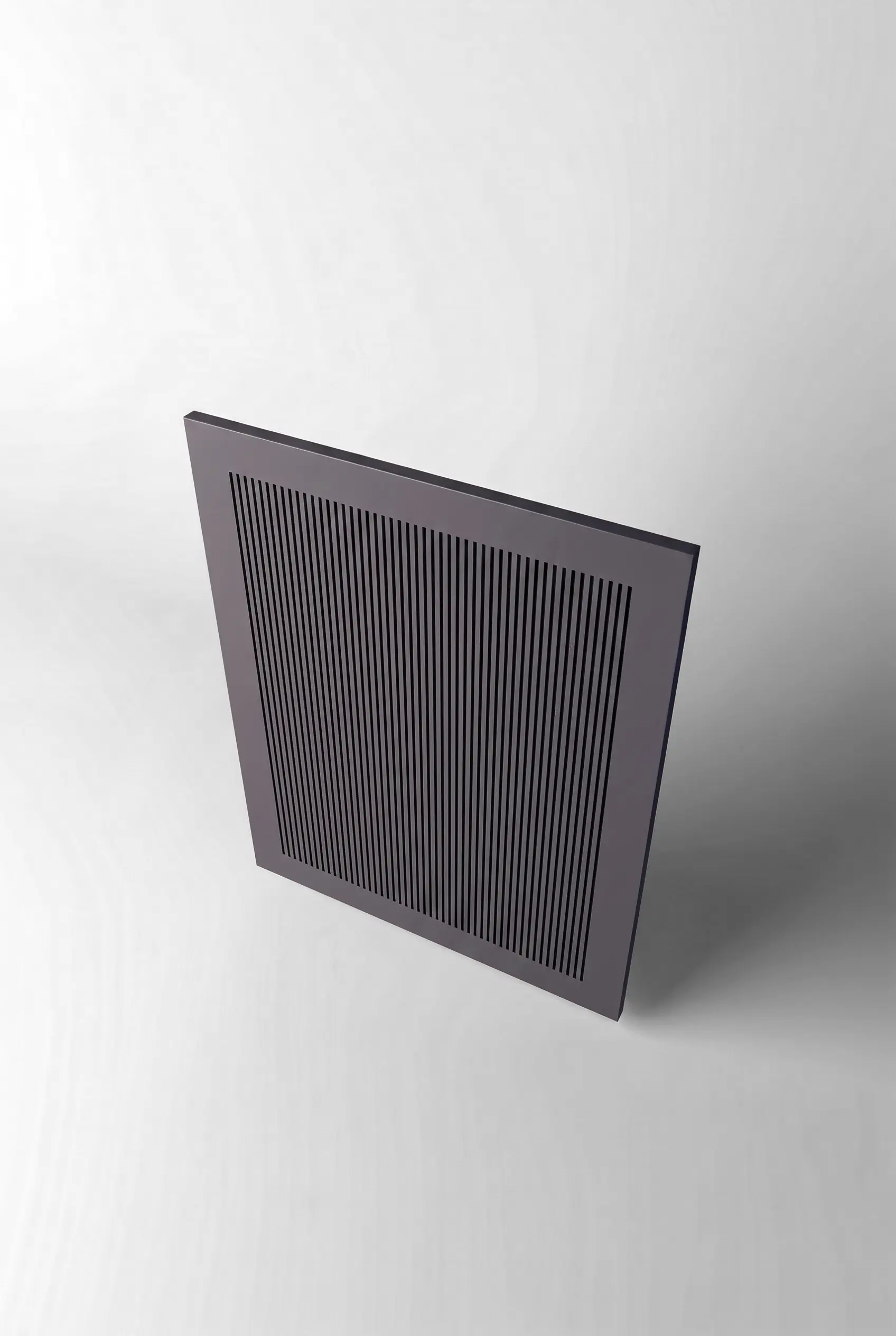 Stiligt - Ett fyrkantigt, svart ventilationsgaller av metall med vertikala slitsar är monterat mot en enfärgad vit bakgrund, sett uppifrån.