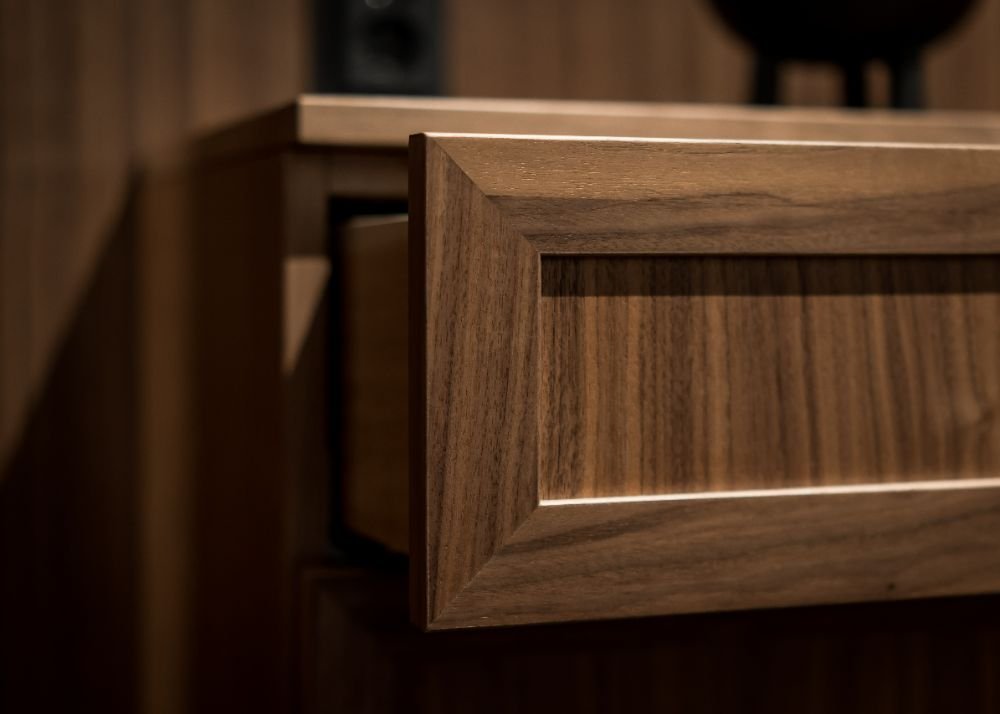 Stiligt - En närbild av en delvis öppen trälåda med en inramad frontpanel, mot en matchande träbakgrund – en detalj som visar det eleganta hantverket som ofta återfinns i platsbyggda klassiska kök.
