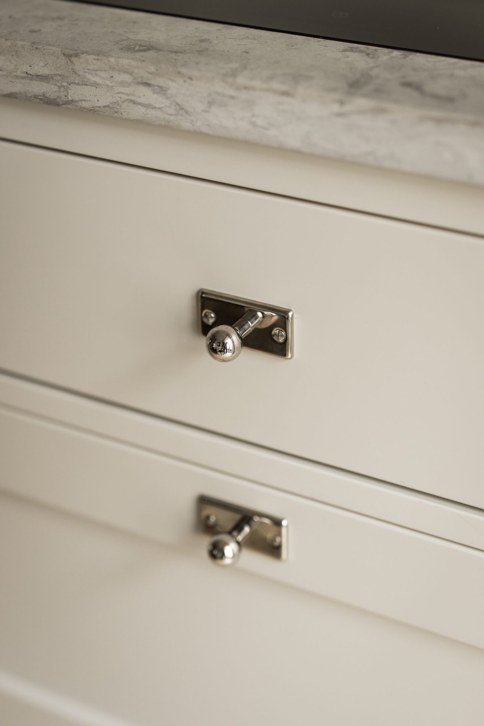 Stiligt - Två krämfärgade lådor i shakerkök-stil med metallknoppar, placerade under en ljusgrå marmorarbetsbänk.
