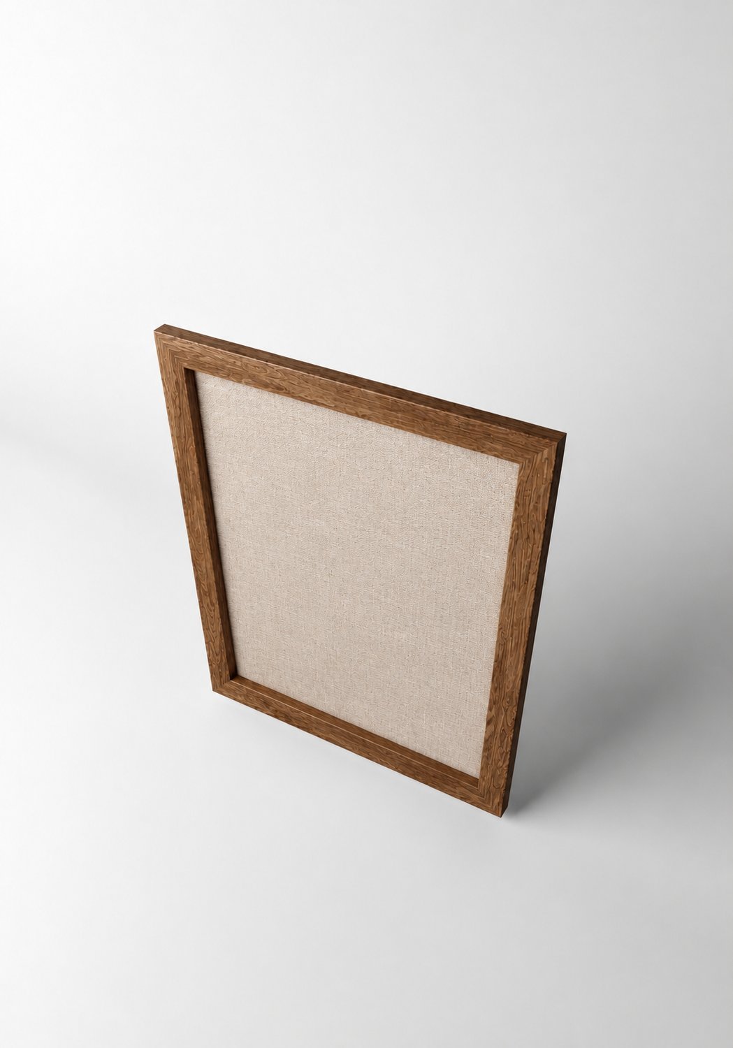 Stiligt - En fyrkantig, tom tavelram av trä med beige duk på baksidan står upprätt på en slät vit yta, sedd från en hög vinkel.