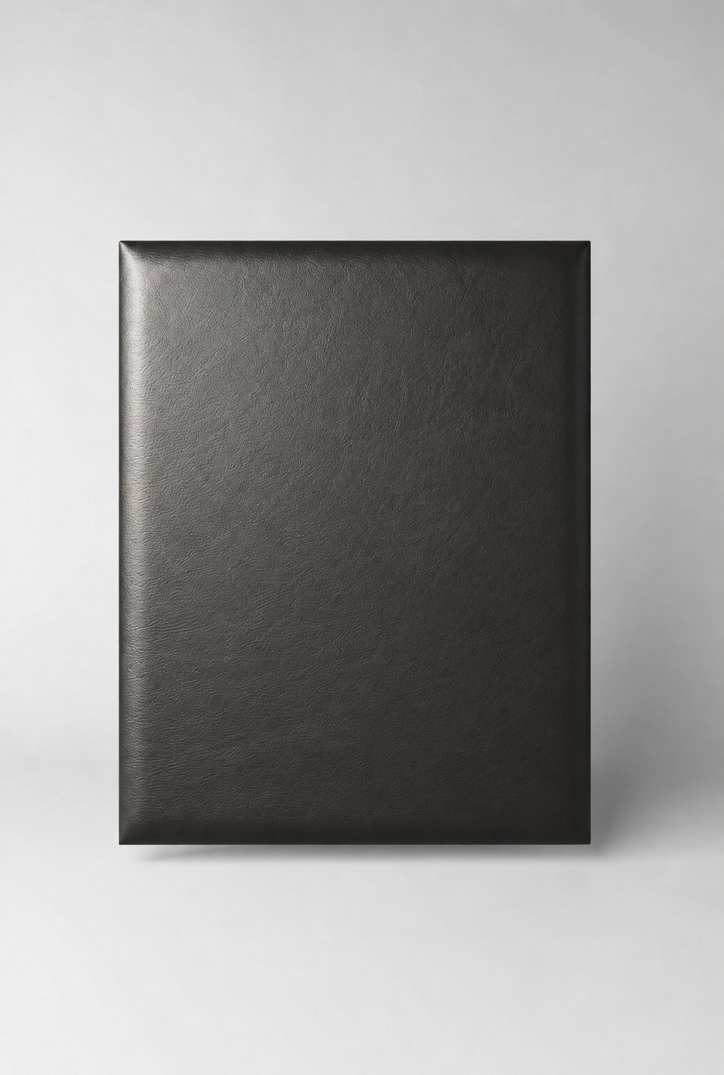Stiligt - En fyrkantig, svart, läderinbunden bok eller pärm står upprätt mot en neutral, ljusgrå bakgrund.